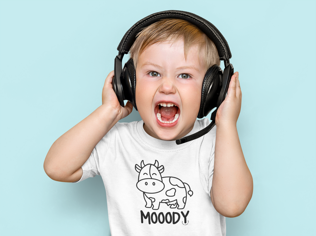 A Moody Toddler Tee featuring a child in headphones, emphasizing comfort and durability for sensitive skin. Made of 100% combed ringspun cotton, light fabric, classic fit, and tear-away label. Ideal for first ventures.