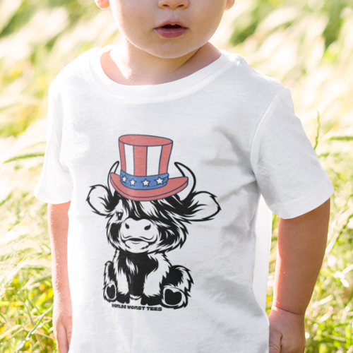 A toddler boy in a white shirt stands in a grassy field. 4th of July Family Cowboy Toddler Tee: soft, 100% cotton, classic fit, tear-away label, perfect for little adventurers.