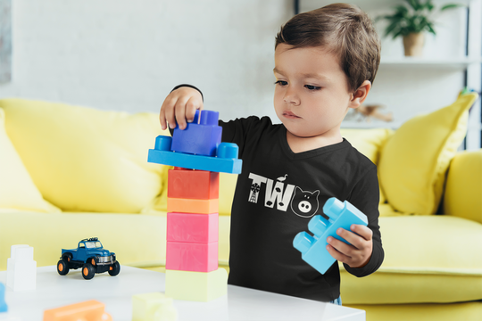 A child playing with blocks, wearing a Two Toddler Tee from Worlds Worst Tees. Made of 100% Ringspun cotton, featuring a classic fit and durable stitching. Ideal for young ones to play in comfort.