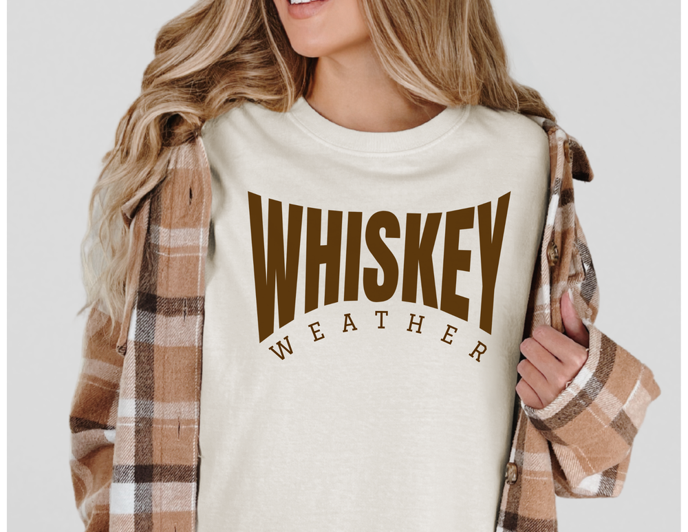 Person models Whiskey Weather Tee under plaid shacket, showcasing bold brown lettering. Comfortable, customizable, relaxed fit tee from Comfort Colors, ideal for casual wear.